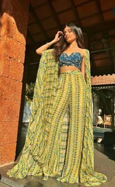 A flowy extravagant cape with simple flared bottom pants and an embellished bustier. This makes for the perfect resort wedding look for a mehandi, haldi, pool party, carnival and welcome lunch. Dress For Pool Party Wedding, Best Indian Outfits Fashion Designers, Mehendi Western Outfit, Casual Indian Dress, Flowy Lehenga Designs, Pool Party Indian Wedding Outfit, Indian Flared Pants, Mehendi Simple Outfit, Dresses For Pool Party Wedding