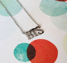 a silver necklace with the word sas on it sitting on top of a polka dot background