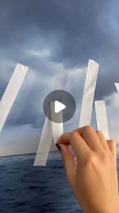 someone is holding paper over the ocean with their thumbnails in front of them