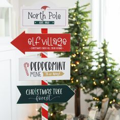 a christmas tree is in the background behind a pole with signs on it that read north pole, elf village and peppermint mine