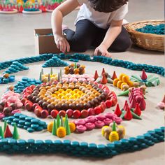 a woman kneeling down on the floor next to a table with many different colored objects