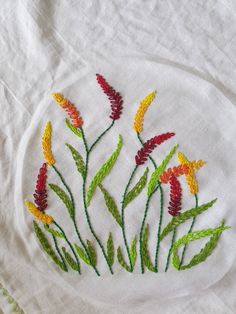 embroidered flowers on a white cloth with green and yellow stems in the center, surrounded by red and yellow leaves