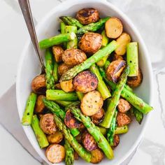 a bowl filled with asparagus and potatoes on top of a white tablecloth