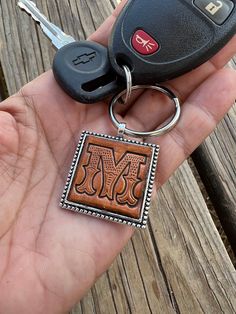 a hand holding a key chain with a wooden block on it and a car keychain