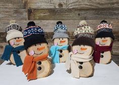 six snowmen wearing hats and scarves are lined up on a white surface with wood planks in the background