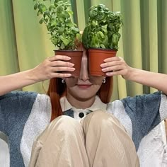 a woman holding two potted plants over her eyes