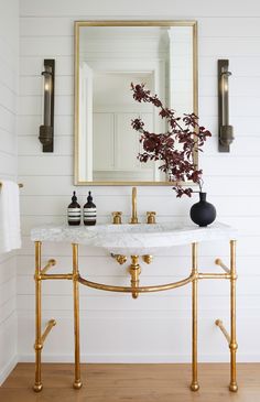 a white bathroom with gold fixtures and a marble counter top, along with a large mirror above the sink