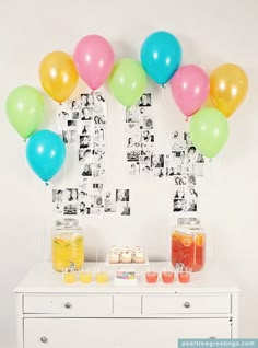 a table topped with lots of balloons next to a white dresser covered in drinks and candies