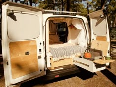 an open white van parked in the woods with it's door open and its bed pulled out