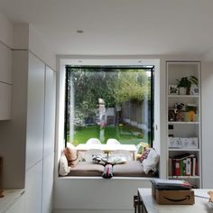 a window seat in the corner of a room with a view of a backyard through it