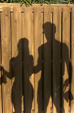 the shadow of two people standing in front of a wooden fence