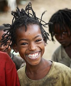 a young boy with dreadlocks smiles at the camera while other children look on