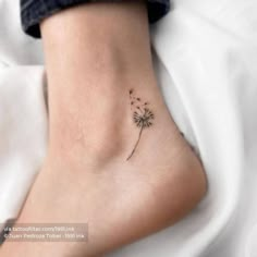 a small dandelion tattoo on the ankle that is sitting on someone's leg