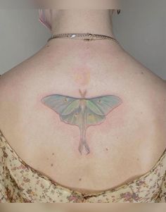 the back of a woman's shoulder with a small moth tattoo on her chest