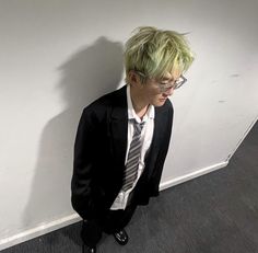 a man with green hair wearing glasses and a suit standing in front of a wall