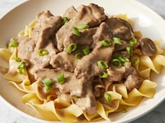 a white bowl filled with pasta covered in gravy and green onion garnish