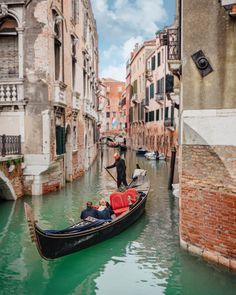 a gondola with two people in it going down a narrow street next to buildings