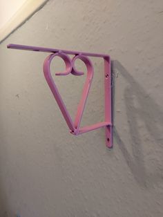 a pink heart shaped sign hanging from the side of a wall next to a white wall