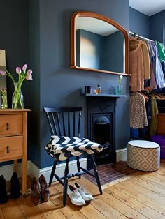 a room with a chair, mirror and shoes on the floor in front of a fireplace