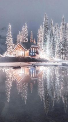 a cabin is lit up in the night with snow on the ground and trees around it