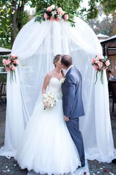 a bride and groom kissing under a wedding arch