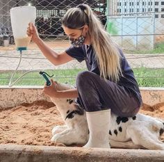 a woman is sitting on the ground with her dog while using a hose to wash it