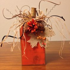 a wooden block with some flowers and leaves in it on a table top next to a white wall