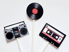 two lollipop sticks with an old school cassette and tape recorder on them, sitting next to each other