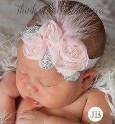 a baby girl wearing a pink flower headband with feathers on it's side