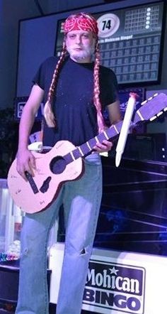 a man with long braids holding a guitar in front of a tv screen and microphone