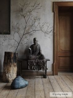 a buddha statue sitting on top of a wooden bench next to a tree branch and rock