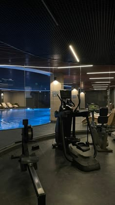 an indoor gym with treadmills, exercise bikes and swimming pool in the background