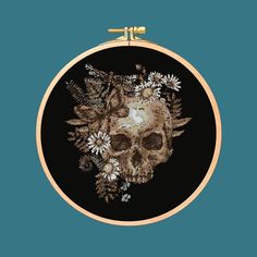 a cross stitch skull with flowers on it's head is hanging from a hoop