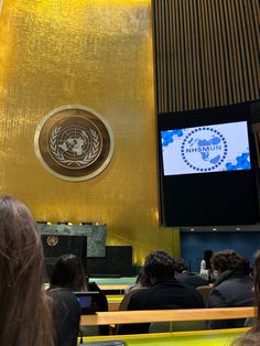 people are sitting on benches in front of a large screen with the united nations logo