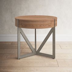 a round wooden table with metal legs on the floor in front of a white wall