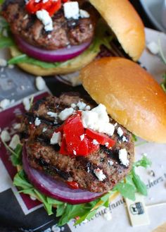 two burgers with onions, cheese and peppers are on the table next to each other