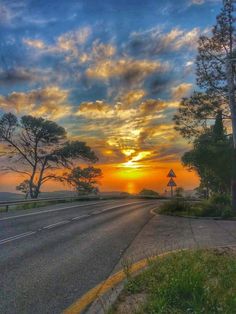 the sun is setting over an empty road