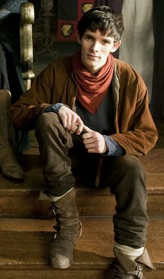 a young man is sitting on the steps wearing boots and a scarf around his neck