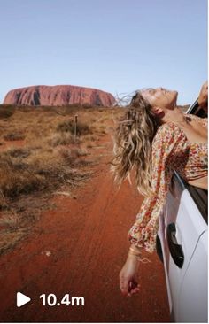 a woman leaning out the window of a car on a dirt road