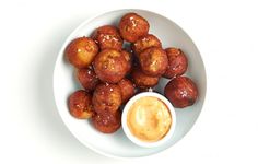 a white bowl filled with fried food next to a cup of dipping sauce on top of it