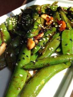 a white plate topped with green beans covered in sesame seeds