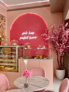 pink chairs and tables in front of a display case with pastries on the wall