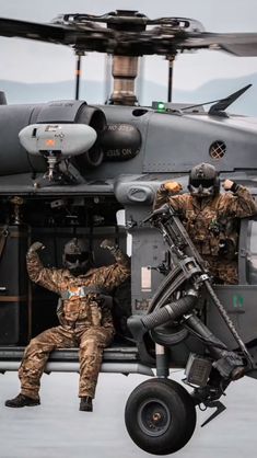 two men in camouflage sit on the wing of an aircraft while another man stands next to it