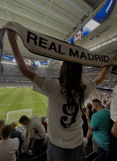 a woman is holding up a real madrid scarf at a soccer game in the stadium