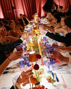 many people are sitting at a long table with wine glasses and flowers on the table