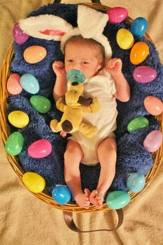 a baby laying in a basket with easter eggs around it