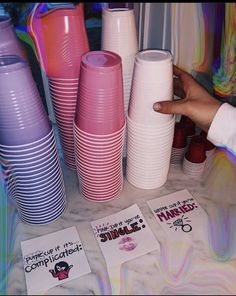 there are many different colored cups on the table and one is pointing at them with a finger