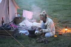 a woman sitting on the ground next to a campfire with a pot full of food