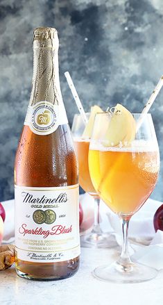 an apple cider and two glasses filled with sparkling peach wine on a marble table