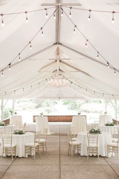 the inside of a white tent with tables and chairs set up for an outdoor wedding